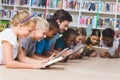 Teacher and kids lying on floor using digital tablet in library Royalty Free Stock Photo