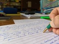 A teacher marking an exam paper at a desk with green pen in hand