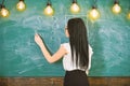 Teacher of mathematics writing on chalkboard, rear view. Lady teacher in glasses explaining formula. teacher