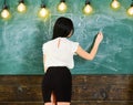 Teacher of mathematics writing on chalkboard, rear view. Lady teacher in short skirt with slit explaining formula