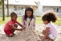 Teacher At Montessori School Playing With Children In Sand Pit