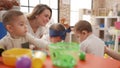 Teacher and preschool students learning to eat sitting on table at kindergarten