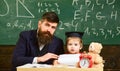 Teacher and pupil in mortarboard, chalkboard on background. Father with beard, teacher teaches son, kid boy. Teaching