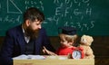 Teacher and pupil in mortarboard, chalkboard on background. Father with beard, teacher teaches son, little boy. Naughty Royalty Free Stock Photo