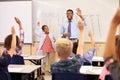 Teacher and pupil with raised hands at front of school class