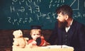 Teacher and pupil sitting in the classroom. Adult man in smart suit is looking to the side while kid is playing with Royalty Free Stock Photo