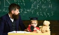 Teacher and pupil sitting in the classroom. Adult man in smart suit is looking to the side while kid is playing with Royalty Free Stock Photo