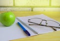 Teacher's Day concept and back to school, green Apple, book, laptop, reading glasses and pen on wooden table, sunlight