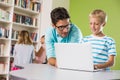 Teacher and schoolboy using laptop in library