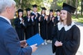 The teacher shakes hands with the student and presents the diploma outdoors. A group of university graduates. Royalty Free Stock Photo