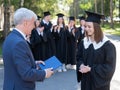 The teacher shakes hands with the student and presents the diploma outdoors. A group of university graduates. Royalty Free Stock Photo