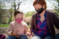 Teacher with small child sitting outdoors in city park, learning group education and coronavirus concept.