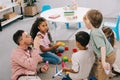 teacher with soap bubbles and multicultural preschoolers sitting on floor with colorful bricks