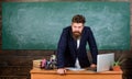 Teacher strict serious bearded man lean on table chalkboard background. Teacher looks threatening. Rules of school