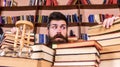 Teacher or student with beard sits at table with books, defocused. Man on frightened face between piles of books, while