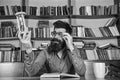 Teacher or student with beard studying in library. Scientist with eyeglasses sits at table and looks at hourglass. Man Royalty Free Stock Photo