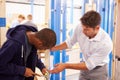 Teacher With Student In Carpentry Class Fitting Door Lock