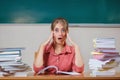 Teacher surrounded by books sitting in school classroom.Emotional teacher at the table. Copy space. Funny photo. Royalty Free Stock Photo