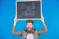 Teacher with tousled hair cheerful about school year beginning. Teacher bearded man holds blackboard with inscription