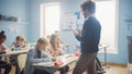 Teacher Uses Digital Tablet Computer While Explainin a Lesson to a Classroom Full of Diverse Child Royalty Free Stock Photo