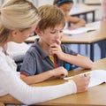 Teacher woman, boy and classroom with book, question and support for education with knowledge at desk. People, learning Royalty Free Stock Photo
