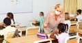 Teacher woman in protective mask helping schoolkid during lesson