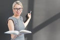 Teacher writing with chalk on blackboard and holding an open book. Royalty Free Stock Photo