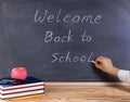 Teacher writing welcome back to school on erased black chalkboard with desktop and supplies in front Royalty Free Stock Photo