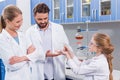 Teachers scientists looking at little student in protective glasses with flask