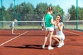 Dark-haired mommy smiling while teaching girl playing tennis