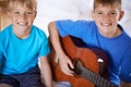 Teaching his brother a few songs...two bothers sitting on a bed with one playing a guitar. Royalty Free Stock Photo