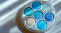 A teal eyeshadow compact rests on a minimalist blue concrete surface, illuminated by soft natural light and surrounded by ample Royalty Free Stock Photo