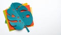 Teal Monstera Leaf Cutout on Colorful Paper Stack on White Surface Royalty Free Stock Photo