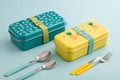 Teal and Yellow Lunchboxes with Utensils on Light Blue Background - generated by ai Royalty Free Stock Photo