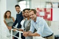 This team aims to succeed. Portrait of a group of smiling coworkers leaning on a railing in an office. Royalty Free Stock Photo
