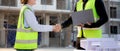 Team architect or engineer holding laptop looking model house and doing agreement while handshake together at construction site, Royalty Free Stock Photo