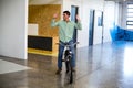 Bicycle rider balancing with hands raised while riding through office corridor, with parked bicycle Royalty Free Stock Photo