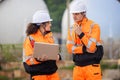 Team of Engineers Collaborating at Industrial Site with Storage Tanks, Industrial Workers Communicating and Using Laptop at Site, Royalty Free Stock Photo