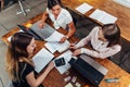 Team of female accountants preparing annual financial report working with papers using laptops sitting at desk in office