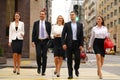 Team of five business people confidently striding along the summer street