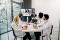 Team of five multiethnical doctors having video conference meeting in hospital with their young African woman doctor Royalty Free Stock Photo