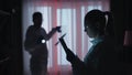 A forensic experts work at the crime scene in a dark apartment lit by red light from police sirens. A man with a knife