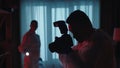 A team of forensic scientists collect evidence at the crime scene, in a dark apartment lit by blue light from police