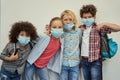We are a team. Four cute multinational kids wearing protective face masks smiling at camera, posing together over light