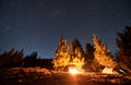 Team of friends resting in campsite on hill under starry sky by campfire. Royalty Free Stock Photo