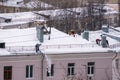 Team of male workers clean roof of building from snow with shovels in securing belts of mantra.