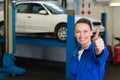 Female mechanic giving thumbs-up in garage with white sedan on lift, red equipment, copy space Royalty Free Stock Photo