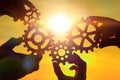 Team of people with gears in hands on sunset background. Royalty Free Stock Photo