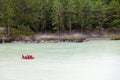 A team of people rafting in orange life jackets on an rubber boat of blue and yellow colors along a mountain river against the