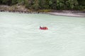 A team of people rafting in orange life jackets on an rubber boat of blue and yellow colors along a mountain river against the